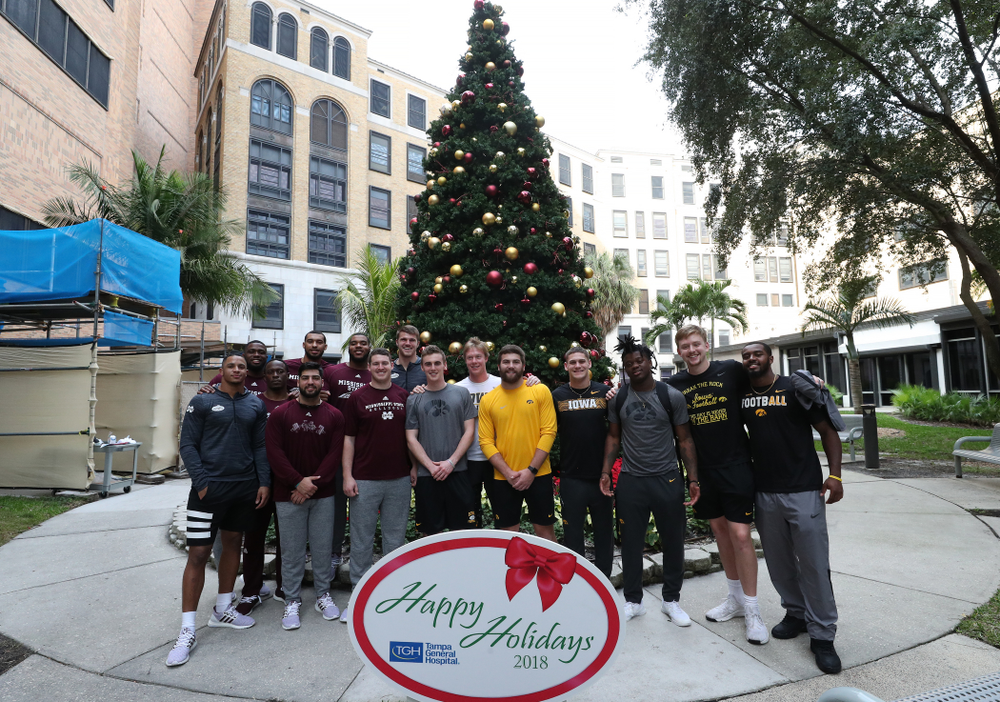 Iowa Hawkeyes tight end Ben Subbert (81), punter Ryan Gersonde (2), wide receiver Max Cooper (19), wide receiver Blair Brooks (83), quarterback Spencer Petras (7), linebacker Jayden McDonald (25), and defensive back Dallas Craddieth (15) pose for a photo with players from Mississippi State during a visit to Tampa General Hospital as part of the Outback Bowl Friday, December 28, 2018 in Tampa, FL.(Brian Ray/hawkeyesports.com)