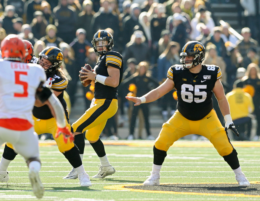 Iowa Hawkeyes quarterback Nate Stanley (4) looks to pass behind a block by offensive lineman Kyler Schott (64) as offensive lineman Tyler Linderbaum (65) looks to block during the second quarter of their game at Kinnick Stadium in Iowa City on Saturday, Nov 23, 2019. (Stephen Mally/hawkeyesports.com)